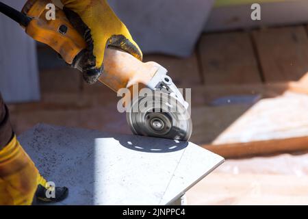 On a ceramic tile floor, a construction worker uses a tool to cut the tiles and lay them with the help of the equipment Stock Photo