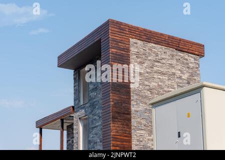 A large outdoor power supply cabinet and substation next to a residential building under construction against the sky. Stock Photo
