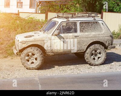 Car completely covered in dried mud is parked on the roadside in the countryside on a sunny day Stock Photo