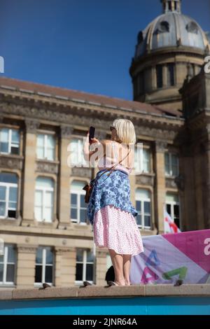 BIRMINGHAM, UK - AUGUST 8, 2022.  An elderly woman using a cell phone to take photographs whilst on vacation in a city environment Stock Photo