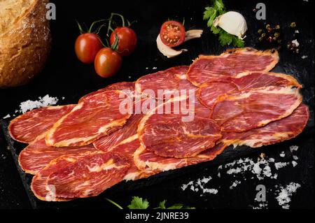 Iberian loin slices on black slate with tomato, parsley, peppercorns and a slice of mushroom Stock Photo