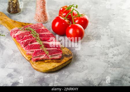 Thin appetizing pieces of bacon on a wooden cutting board, fresh tomatoes, spices in glass jars on a white background. Healthy lifestyle, delicious or Stock Photo