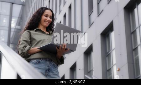 Successful 30s businesswoman working typing on laptop using free city Wi-Fi chatting on wireless computer standing near office company building female Stock Photo