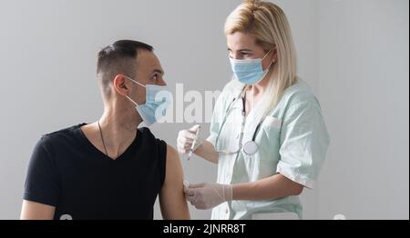 woman doctor in a protective face mask makes vaccination to european man in hospital Stock Photo