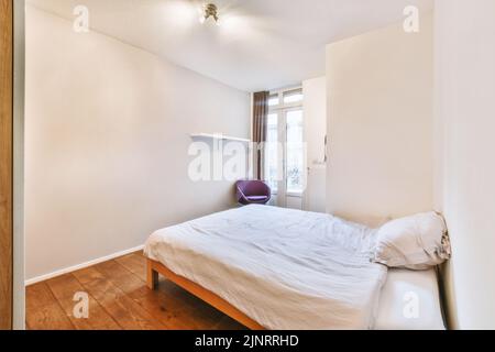 Comfortable bed with ornamental blanket placed near glass door and wardrobe in light bedroom Stock Photo