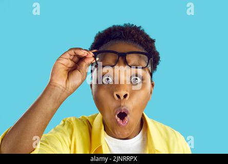 Funny surprised young woman looking at you with shocked expression on light blue background. Stock Photo