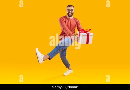 Portrait of happy smiling young man with gift box dancing on yellow studio background Stock Photo
