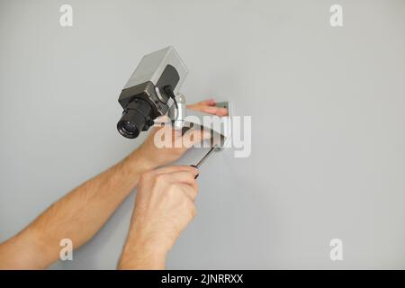 Hands master man mount camera for surveillance in anti-vandal metal case on wall inside building Stock Photo
