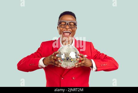 Young African American man entertainer in stylish glasses and red suit clutches disco ball for party Stock Photo