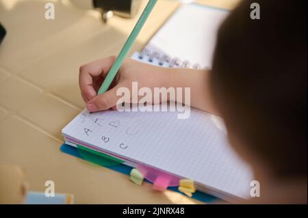 View from above with details on hand of a schoolchild, first grader learning the writing, writes letters in a copybook Stock Photo