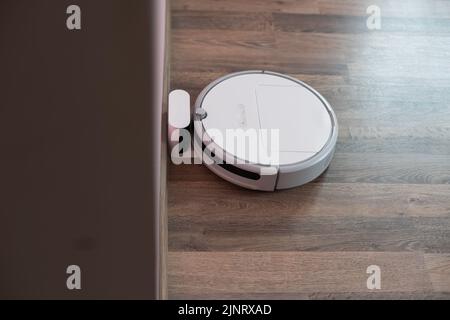 Robotic vacuum cleaner on laminate wood floor charging from base station. Smart cleaning technology. robot vacuum cleaner return to charging at dock Stock Photo