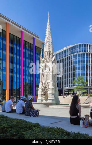 People take a rest and watch the world go by in Chamberlain Square. The Chamberlain Memorial erected in 1880 juxtaposed with contemporary architecture. Stock Photo