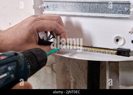 An electrician fixes ends of wires in brass distribution bar using an electric screwdriver. Stock Photo