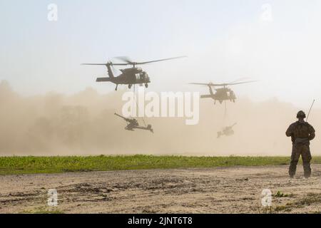 An Ohio Army National Guard Soldier watches UH-60 Black Hawks, assigned to 1st General Support Aviation Battalion, 111th Aviation Regiment, carry M119A3 Howitzers, belonging to 1st Battalion, 134th Field Artillery Regiment, during Operation Northern Strike at Camp Grayling, Mich., Aug. 8, 2022. Participants of Northern Strike operate in a multidomain, combined joint environment to improve their Joint All-Domain Command and Control capabilities by integrating legacy and modern equipment with future innovation. Stock Photo