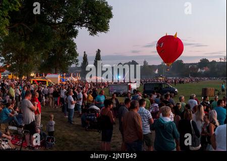Heldburg, Germany. 13th Aug, 2022. Numerous people have come to the atmospheric balloon glow at the fairground. The 25th Thuringian Montgolfiade, the German championship in hot air ballooning, takes place in Heldburg. Of the 58 hot air balloons registered, 33 are taking part in the competition. Credit: Daniel Vogl/dpa/Alamy Live News Stock Photo