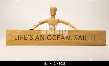 The word Life's an ocean, sail it written on wooden surface. Slogans and positive thinking Stock Photo
