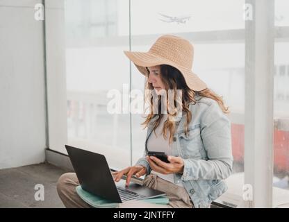 Woman using devices near airport window Stock Photo