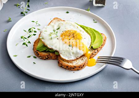 Avocado toast on a toasted multigrain bread with a fried egg Stock Photo