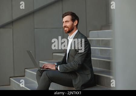 Focused Businessman working on laptop sitting on stairs outside office building  Stock Photo