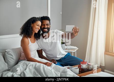 Lets take a selfie of our breakfast in bed. Cropped shot a young attractive couple taking a selfie while having breakfast in bed at home. Stock Photo