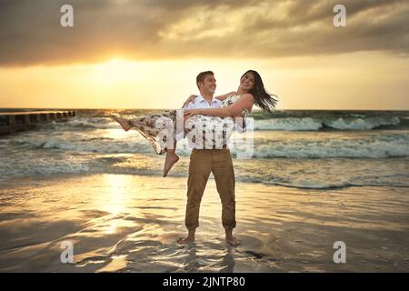 He always lifts me up. Full length shot of a handsome young man carrying his girlfriend on the beach. Stock Photo