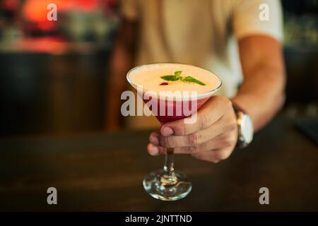 This ones on the house. Closeup of an unrecognizable barmen putting down a cocktail on the counter he just made inside of a restaurant during the day. Stock Photo