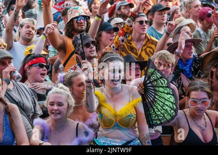 Crowds of youngsters in costumes seen singing and dancing at the Fair Festival. BoomTown Festival - Chapter 1: The Gathering - takes place at Matterley Estate, near Winchester, Hampshire, and will run from Wednesday 10th until Sunday 14th August 2022. Boomtown follows a storyline that evolves each year, and has been reset for the post-pandemic world where the State of Emergency has become a State of Emergence that has risen from the ashes of the old. It is a new world, accompanied by a new story that is waiting to be told that focuses on reflection, acceptance and reconnection. It is a time of Stock Photo