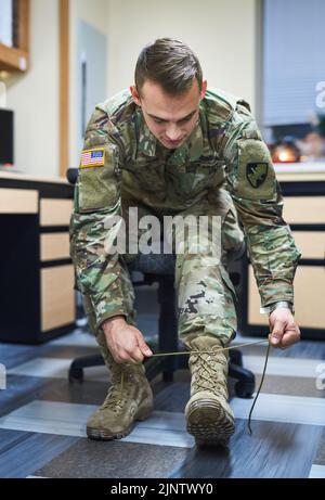 Battle is better in boots. a young soldier tying his boot shoelaces in the dorms of a military academy. Stock Photo