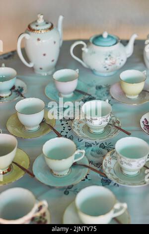The table is set, time to begin the tea party. tea pots and tea cups laid out on a table at a tea party inside. Stock Photo
