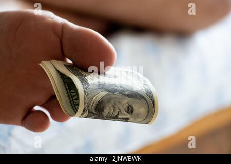 Man's foot holding one hundred dollars with toes lying on the bed at home, passive income, business and work, leisure and money, money in feet Stock Photo