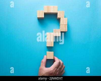 Hand placing a wooden block to complete a question mark shape on a blue background Stock Photo