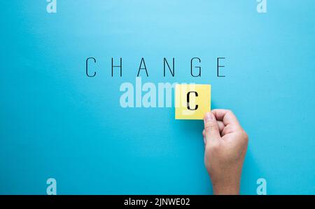 Hand placing yellow sticky note with letter c to spell change on blue background Stock Photo