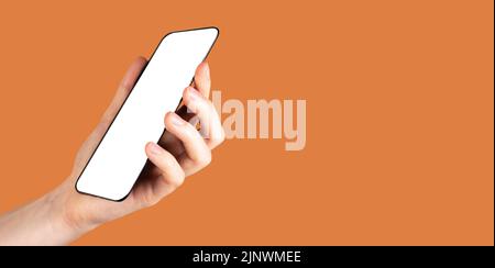 Banner with hand holding phone mockup on orange background. Angled view. Android template with white screen. Copy space. High quality photo Stock Photo