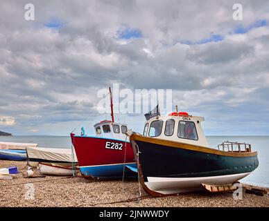 Small traditional fishing boats hauled up on the stony shingle beach in Beer, a small coastal village in Devon on the Jurassic Coast Stock Photo