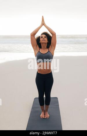 Young woman standing on a mat at the beach practicing yoga Stock Photo