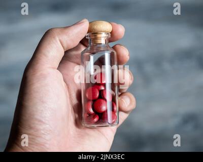 Close up red vitamins or supplements in the small clear glass bottle vials in person's hand. Hand holding vials with drug pills capsules. Healthcare, Stock Photo