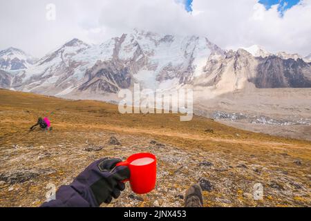 Man lying on a hill with a cup of fresh milk of Yakmu (female of Yak animal) ,view of mountains and sky in Gorakshep village - Nepal, Everest Base Cam Stock Photo