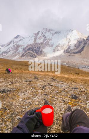 Man lying on a hill with a cup of fresh milk of Yakmu (female of Yak animal) ,view of mountains and sky in Gorakshep village - Nepal, Everest Base Cam Stock Photo
