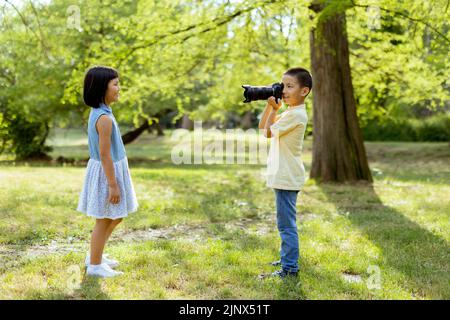 Cute little asian boy acting like a professional photographer while taking photos of his little sister Stock Photo