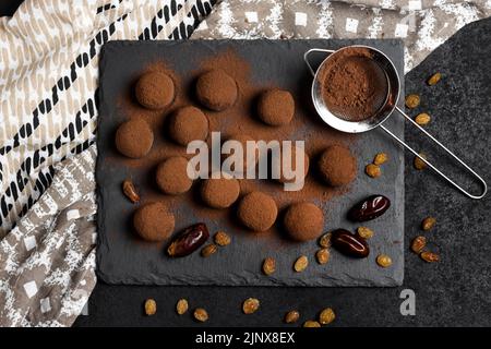 Homemade vegan truffles with dried fruits, walnuts and raw cocoa powder served on black slate plate. Flat lay, top view. Stock Photo
