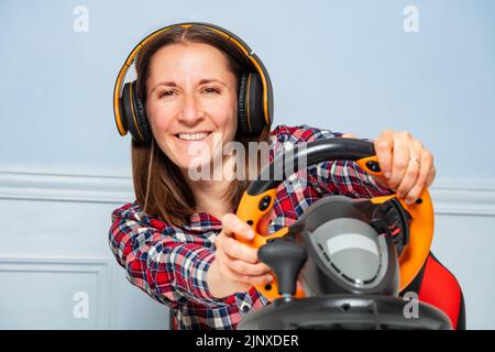 Woman gamer in headphones playing race game with steering wheel Stock Photo