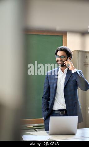 Smiling young indian business man wearing suit talking on phone at workplace. Stock Photo