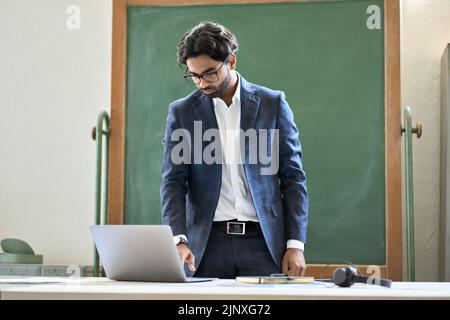 Young indian business man working on laptop computer standing in office. Stock Photo
