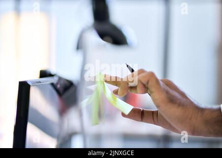 Business man hand putting sticky note reminder on pc computer working in office. Stock Photo