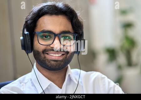 Smiling indian business man wears headphones looks at camera, headshot portrait. Stock Photo