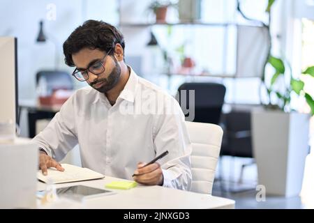 Busy indian professional business man working at office desk sit at workplace. Stock Photo