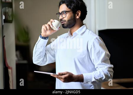 Smiling rich successful indian business man drinking coffee in morning at work. Stock Photo