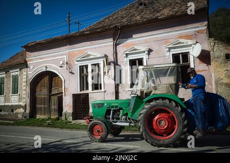 Man in blue boiler suit sending a text message as he catches a ride home on the back of a tractor in Transylvania Stock Photo