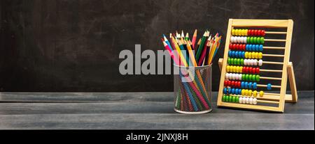 Back to school template. Colorful pencils and Abacus on classroom blue wooden desk, blackboard background, copy space Stock Photo