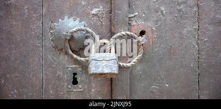Old vintage wooden door locked with rusty padlock on metal double handle. Close up view of keyhole and safe closed entrance with padlock. No access co Stock Photo